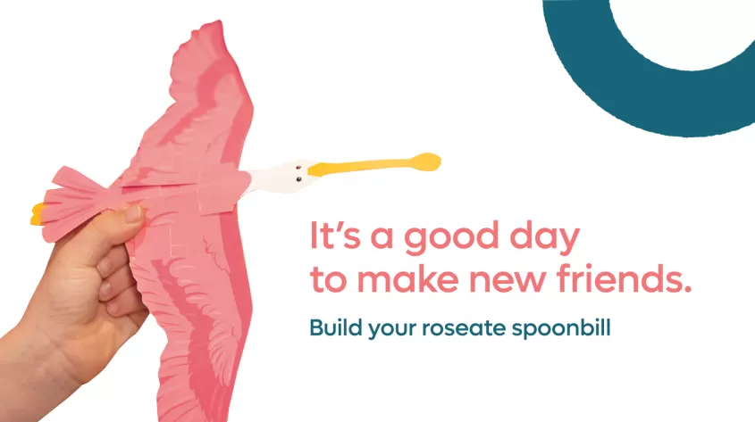 A person holds the paper cutout Spoonbill with the following copy: It's a Good Day to make new friends.