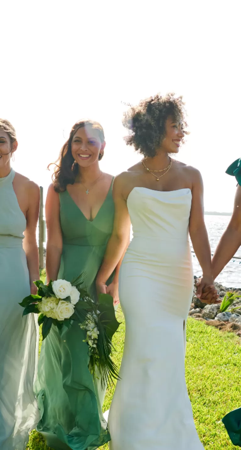 a group of bridesmaids hold hands and walk alongside the river