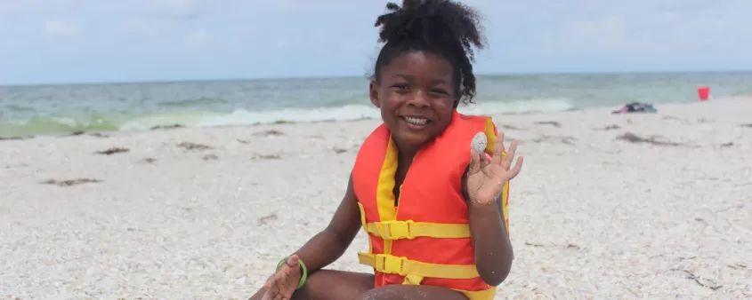 A close-up of a child or person crafting with seashells on a sunny beach